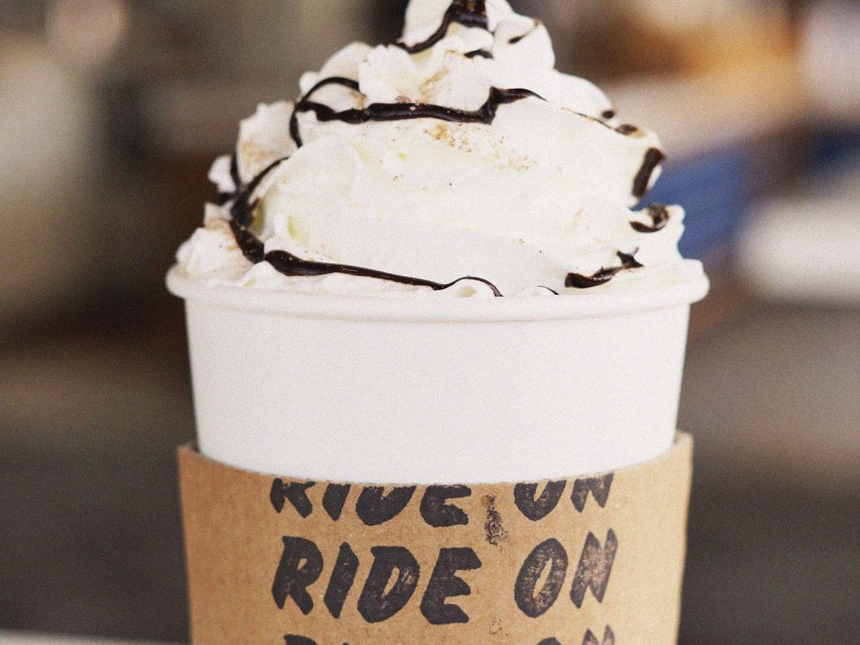 Hot coffee topped with whipped cream and chocolate syrup with branded sleeve