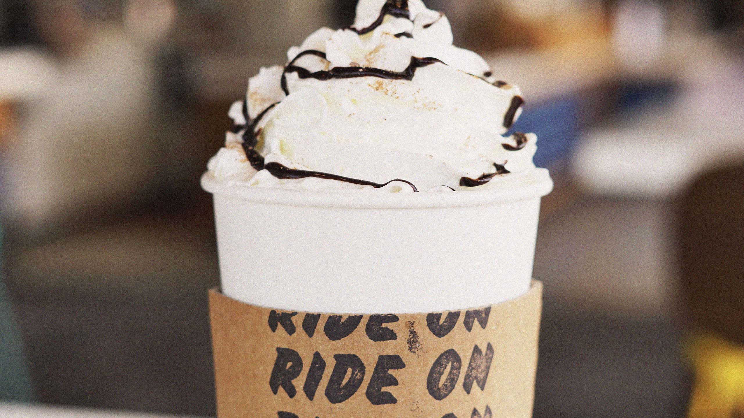 Hot coffee topped with whipped cream and chocolate syrup with branded sleeve