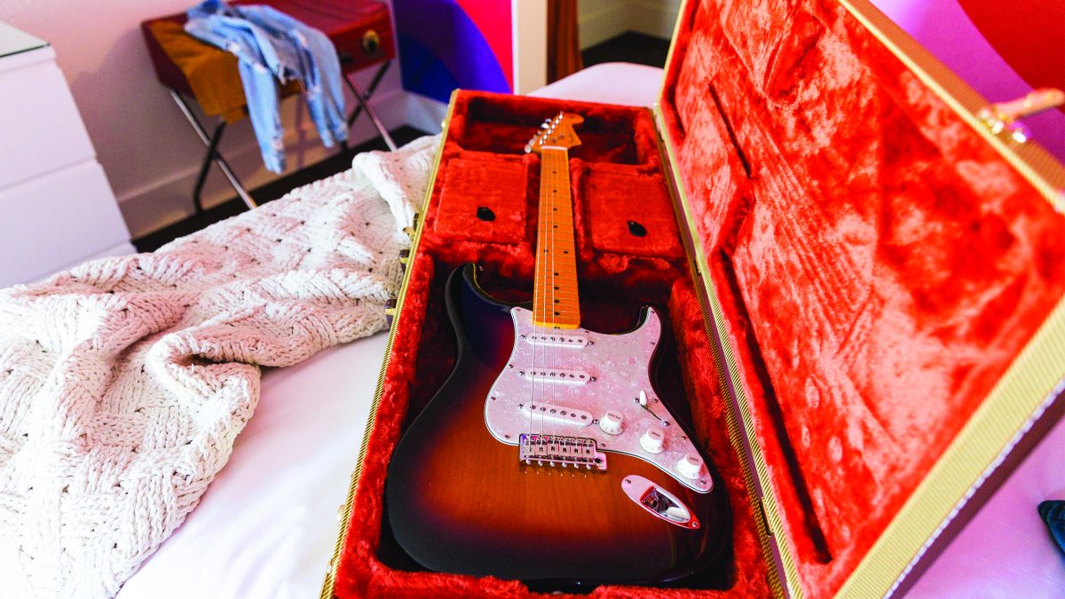 Brown electric guitar in its case on a bed in a guest room of the Rambler Motel