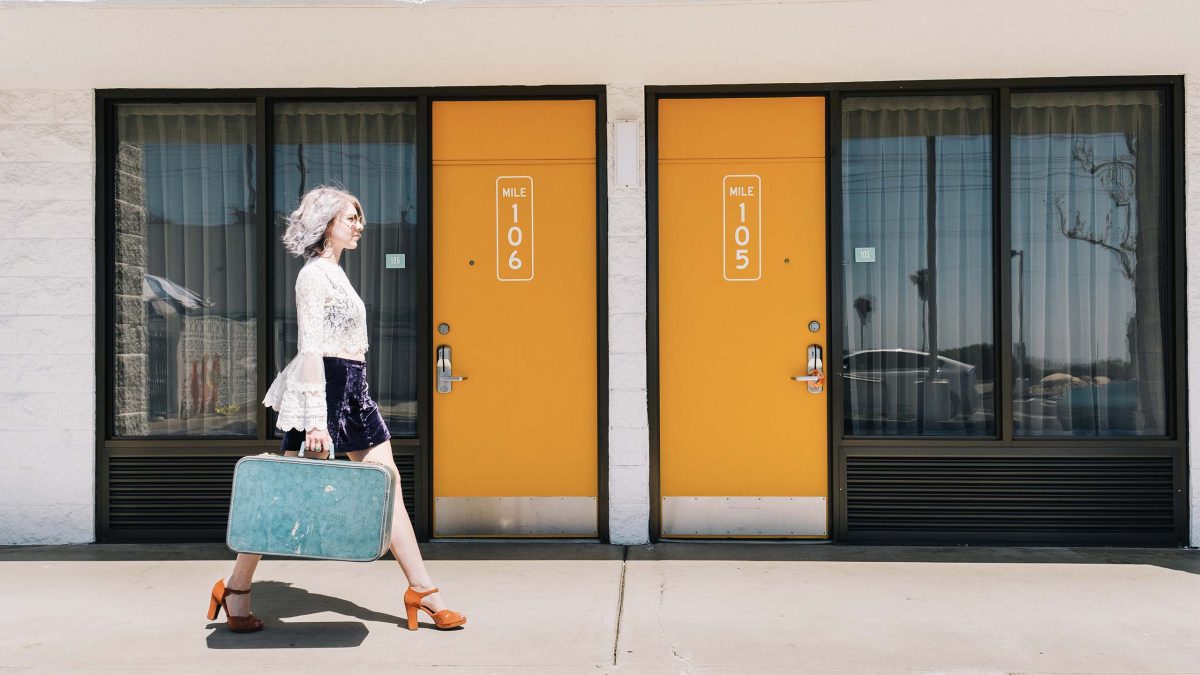 Woman with blue suitcase walking past the Rambler Motel doors