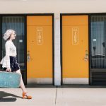 Woman with blue suitcase walking past the Rambler Motel doors