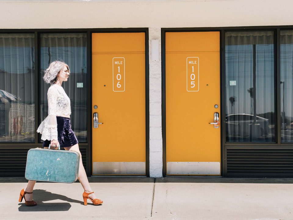 Woman with blue suitcase walking past the Rambler Motel doors